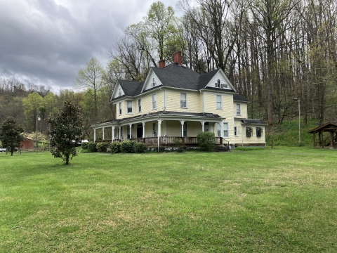 A photo of a large Victorian house. The house is a pale yellow, and has a wrap-around porch.