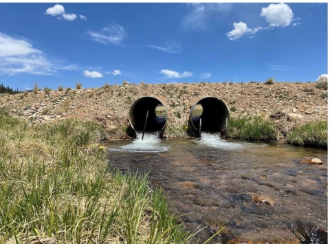 Two pipes positioned in the center of a stream, with water flowing around them.