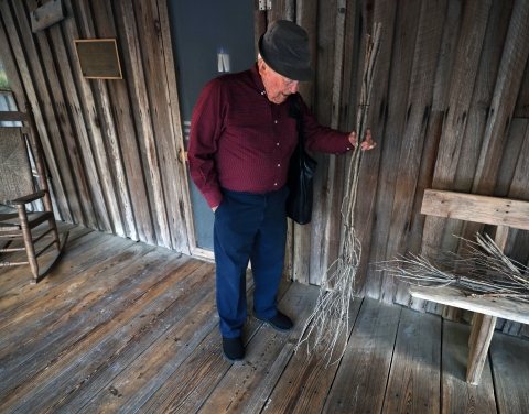 Standing on the front porch holding a broom made of small tree branches, Joe shows how his family set the floor planks a half inch apart on the raised house frame so they could easily sweep dirt and sand through the gaps and onto the ground below the house.