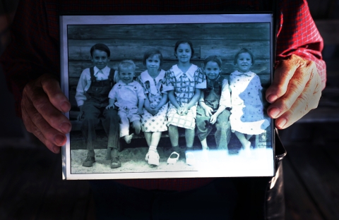 Photo shows Joe Chesser's hands holding an old black and white photo of his brothers and sisters as children.