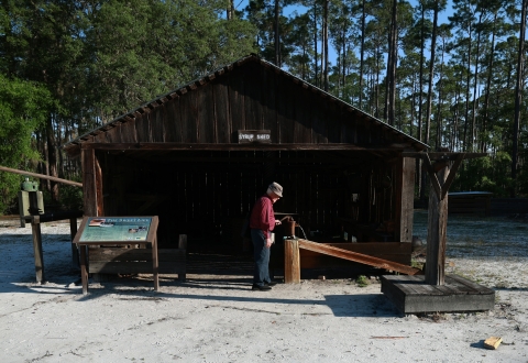 Joe Chesser stands in front of the old syrup shed pumping water from the still working hand pump.