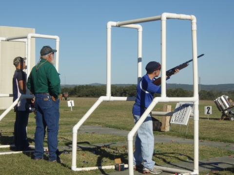 Boy aims sporting rifle at targets while standing behind a mobile range stand. 