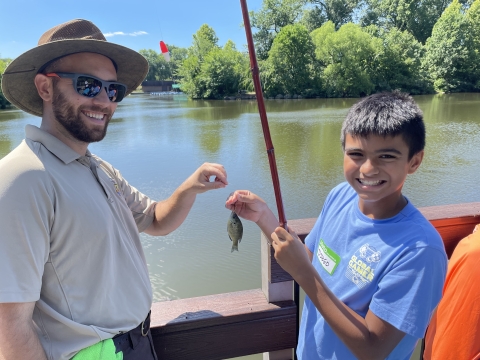 Youth poses with a fish he caught with the assistance of U.S. Fish and Wildlife Service staff member Jason Vassallo