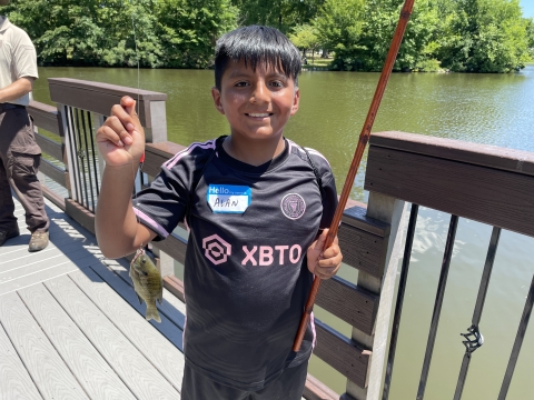 Youth poses with a fish he caught at the 2024 Cops and Bobbers fishing program as part of the Elizabeth Urban Wildlife Refuge Program