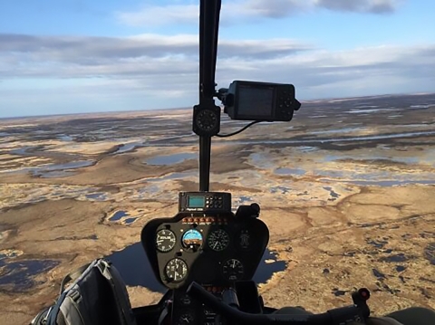 From a helicopter cockpit, brown wetlands and jeweled lakes stretch across the land below.