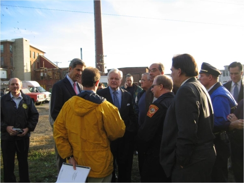 a gathering of people outdoors with an old factory in the background