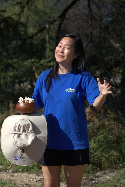 Woman standing with coral offering in wood bowl