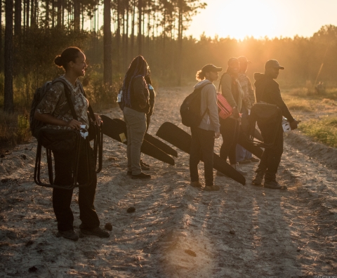 Fort Valley State University students, dressed for hunting, stand on dirt road at sunrise.