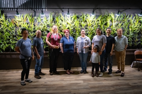 Members of the San Diego Zoo Wildlife Alliance gather for a photo in front of a plant wall at the Maui Bird Conservation Center. The awardee, Jennifer Pribble, is wearing a lei and holding an engraved bowl.