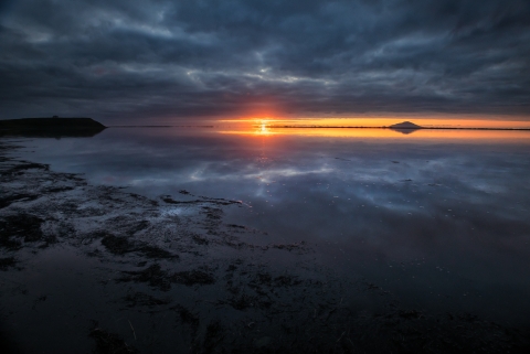 Sunset over calm water with dark clouds reflected