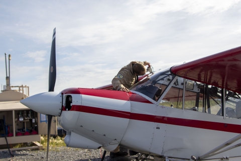 FWO Cody Smith with a fuel hose putting fuel into the wing tanks of a Top Cub bush plane with a remote fuel station in the background.