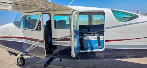 Side shot of small prop plane with blue coolers with white lids containing woundfin are loaded inside.