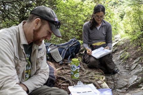 Two biologists beside a trail with clipboards and papers