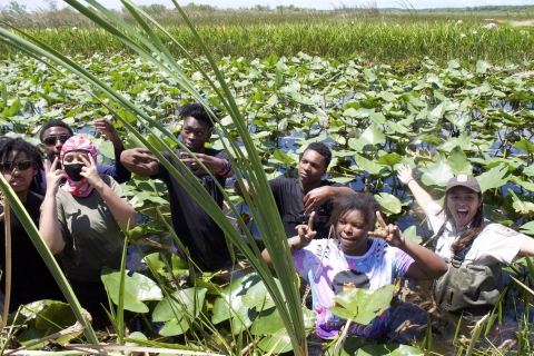 Six teenagers and a uniformed FWS staff wade waist deep into the water and exclaim joyously.