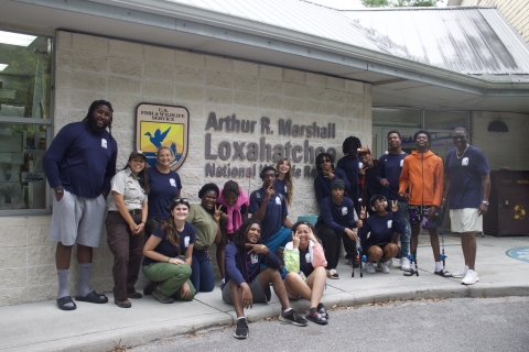 An array of students and staff pose in front of a building with a sign saying “Arthur R. Marshall Loxahatchee National Wildlife Refuge”