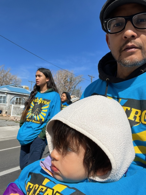 3 adults in bright blue T-shirts walk down street; one holds child