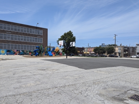 an asphalt schoolyard with basketball hoops and a playground