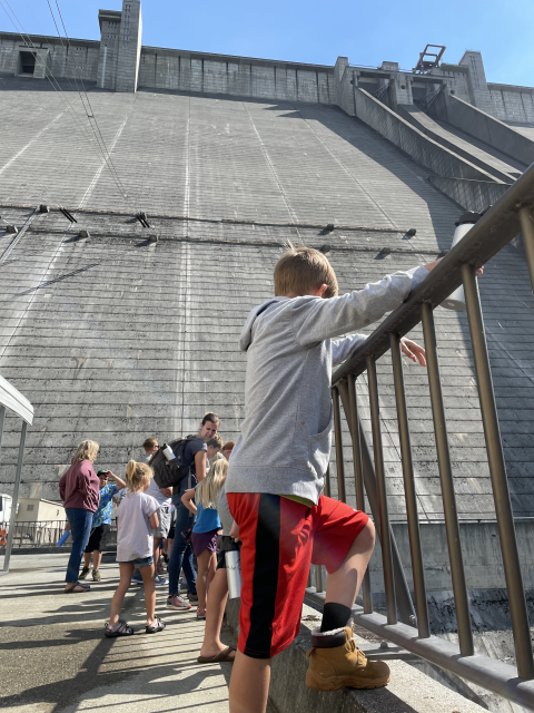 Several kids standing at the base of a dam on a summer day.
