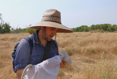 A man in a large straw hat holds a net and looks down at it.