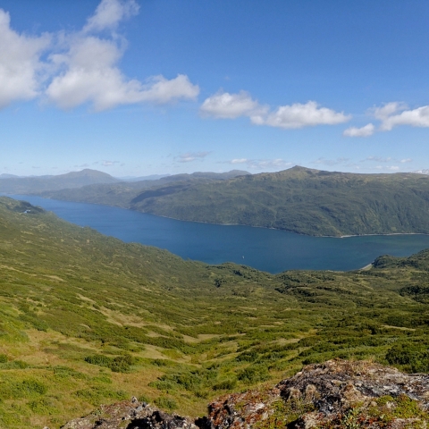 Cerulean blue water stretches between sloped mountains beneath a partly cloudy sky.