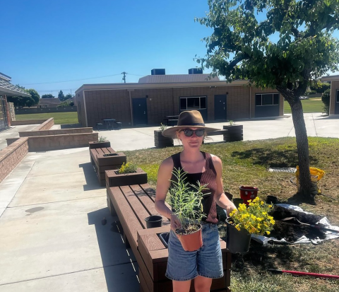 A woman wearing a hat and sunglasses holding a potted plant in each hand