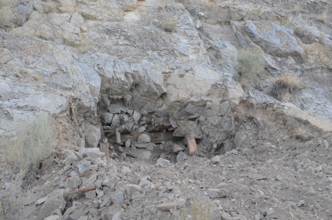 A depression in a rocky hill can be seen surrounded by dirt and rock.