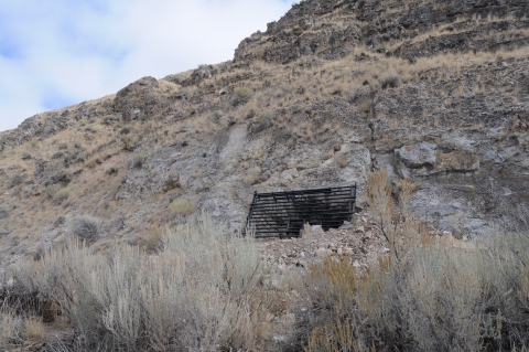 In a rocky landscape, a metal grate can be seen covering a mine adit.