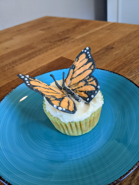 A monarch butterfly cupcake topper made out of royal icing, sitting atop a vanilla cupcake