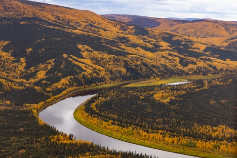 A river bend reflecting a partly cloudy sky, winding through mountains covered in orange and green trees and tundra.