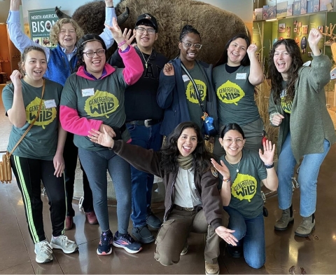 A group of people smiling and posing while standing in front of an American bison display in an education center.