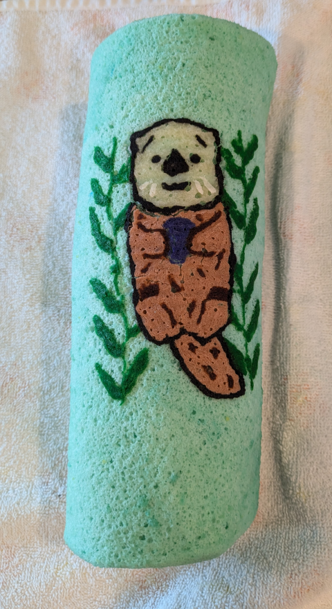 A light blue swiss roll cake with featuring a sea otter design