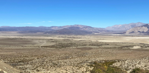 Aerial view of an arid shrubby landscape with mountains in the background