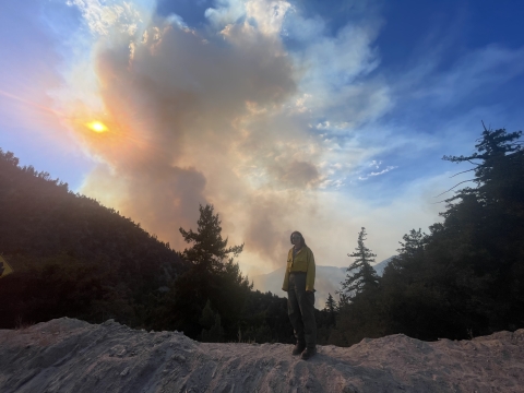 a woman stands on a ridge in front of a smokey and mountainous landscape