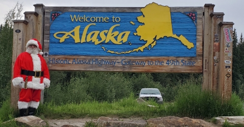 Watercraft inspector, Steve Wogtech, posed in Santa suit in front of Welcome to Alaska sign.