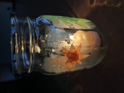 A canning jar decorated with tissue paper cutouts representing a star, tree and sun