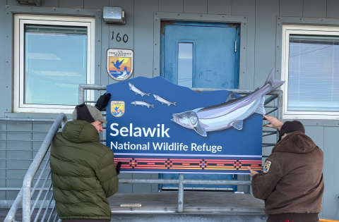 Two men hold up a blue refuge sign in front of a building