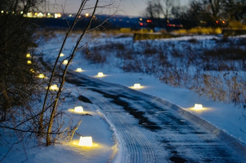 snowy path lit up with small candles on the sides of the path