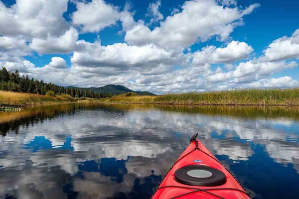 A bright blue sky obstructed by fluffy white clouds reflected off of a stream shot from inside a kayak