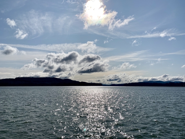 Blue water stretches out to the horizon under distant dark mountains and white clouds