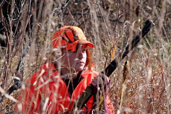 hunter dressed in hunter orange crouches in the bushes