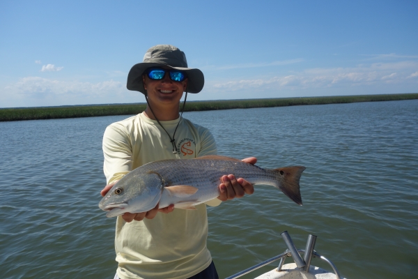 Angler stands in a boat in the estuary and holds large spottail bass he caught.