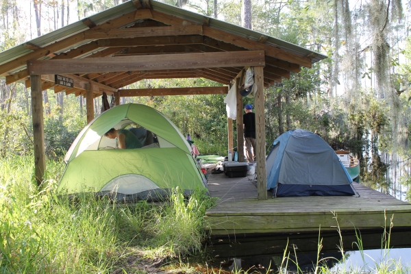 Grass in the foreground with a green and blue tent on a platform with a roof