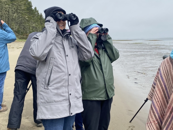 Two people standing holding binoculars up to their eyes. 