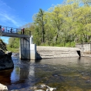 A dam crosses a river, but a portion has been removed to that water can flow through. People stand on an overlook that crosses the open section of the river. 