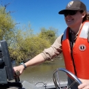 A woman drives a boat wearing a life vest and Fish and Wildlife Service hat