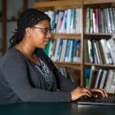 Liberian working on laptop with bookshelf in background