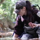 Female biologist kneeling in the water, one hand in the water, the other, cupped, holding mussels