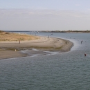 A beach peninsula on an overcast day, with dozens of fishermen in the water.