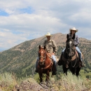 Two horseback riders in the mountains pose for a picture.