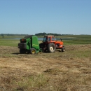 An old, red, closed-cab tractor pulls a green round-baler on a waterfowl production area.